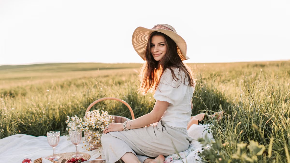 A young woman relaxing during a summer picnic in a sunlit field, surrounded by fresh fruits and flowers.